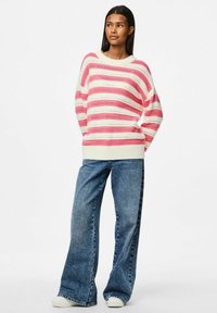 Pull en tricot avec des rayures horizontales roses et blanches, doté d'un col et d'un ourlet côtelés. Associé à un jean bleu à jambes larges et des baskets.