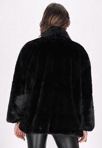 Jachetă din blană artificială neagră, cu guler lat, croială oversized și textură netedă. Membre lungi și un aspect moale, pufoș.