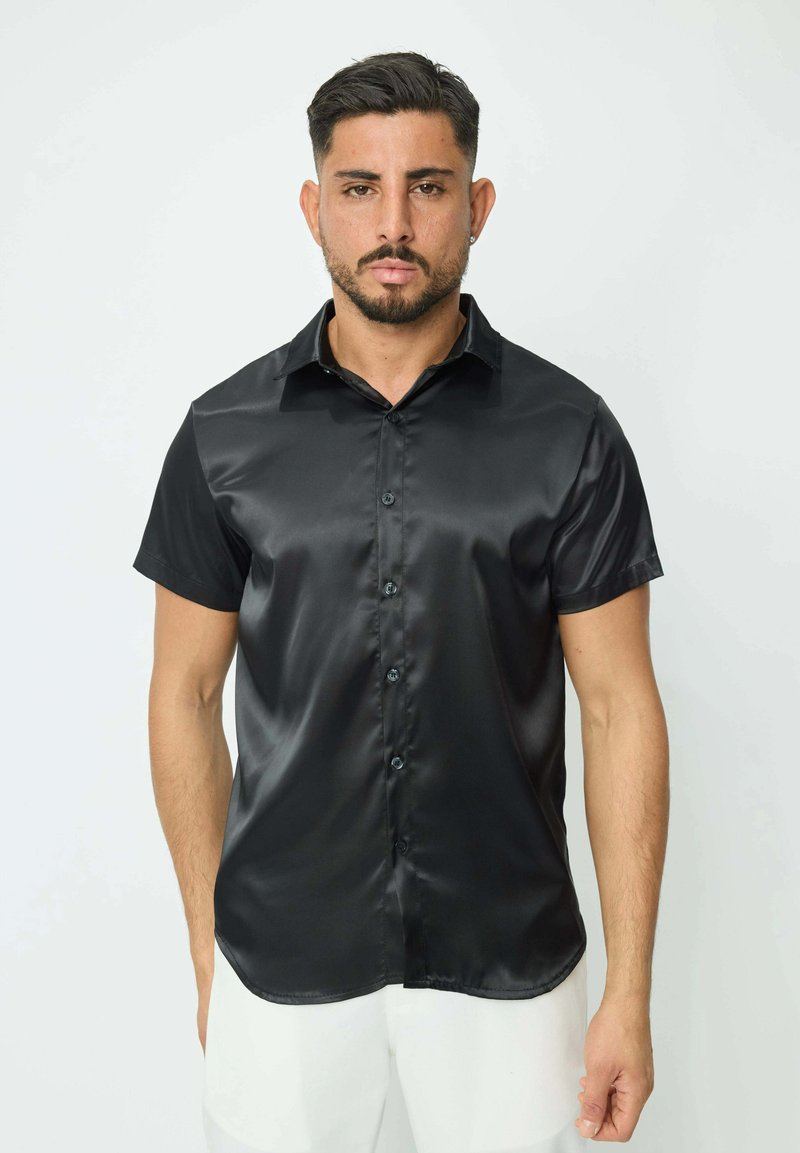 Chemise noire à manches courtes en tissu brillant, avec un devant à boutons et un col pointu. Coupe droite au bas de l'ourlet.