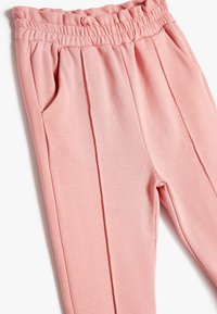 Pantalones de color rosa claro con cintura elástica, con pliegues y bolsillos laterales. Están hechos de una tela suave con una textura lisa.