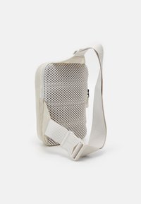 Beige rektangulär axelväska med en texturerad mesh-framdel, dragkedjestängning och justerbar bred rem med en plastspänne.