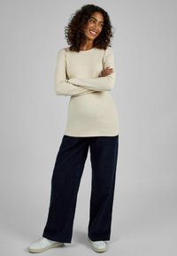 Lichtbeige langemouwen top, gecombineerd met wijde marineblauwe broek. De top heeft een ronde halslijn en de outfit wordt afgemaakt met witte sneakers.
