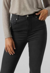 Jeans negros de cintura alta, hechos de denim elástico, con bolsillos frontales, cierre de botón y una silueta ajustada y elegante.