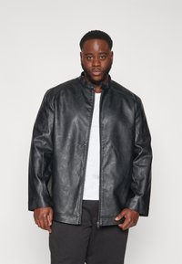 Chaqueta de cuero sintético negra con cuello alzado, cremallera frontal y mangas largas. Presenta una textura suave y un corte entallado.