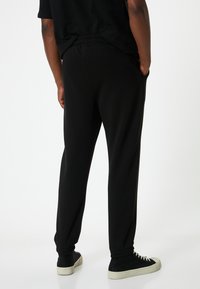 Sorte sweatpants med elastisk talje og manchetter. Har sidelommer og en glat, blød stoftekstur. Sammen med sorte sneakers.