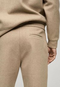 Béžové vlněné tepláky s jemnou texturou, so slim fit, elastickým pásom a jednou zadnou vreckom na pravej strane.
