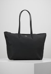 Sac fourre-tout noir en tissu texturé, doté de deux longues poignées et d'une fermeture éclair. Détail de petit logo sur le devant.