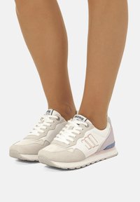 Sneakers bianchi e beige realizzati in materiali scamosciati e in rete, con un design testurizzato, lacci e un accento di colore viola chiaro sul tallone.