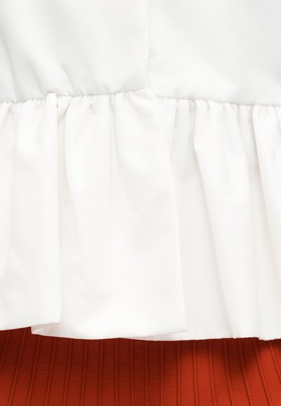 Λευκό ύφασμα με λεπτομέρεια ραφής που συγκεντρώνεται πάνω από μια υφασμάτινη επιφάνεια με φολιδωτή υφή σε σκουριασμένο χρώμα.