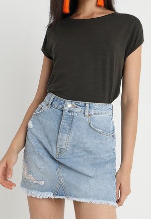 Frau trägt schwarzen Top mit hochgekrempelten Ärmeln und hellblauem, verwaschenem Denim-Minirock mit ausgefranstem Saum sowie orangefarbene Quasten-Ohrringe.