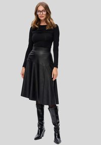 Czarna bluzka z długim rękawem i marszczeniami, wysoka spódnica z czarnej skóry, oraz czarne kozaki do kolan na słupku, wszystko prezentowane na modelce.