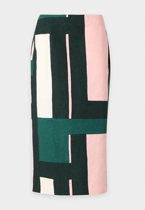 Femme aux longs cheveux blonds portant un crop top sans manches à motif géométrique et une jupe midi assortie avec des chaussettes et des chaussures plates, debout sur un fond blanc.