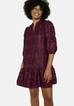 Burgundy dress featuring textured fabric with floral patterns, a v-neckline, and three-quarter sleeves, finished with a ruffled hemline.