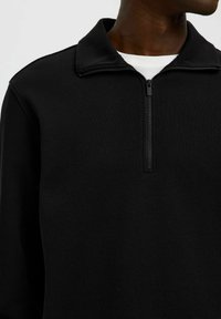 Zwarte kwart-rits pullover van textuurstof, met een effen kraag en een voorrits, met een eenvoudig en minimalistisch ontwerp.
