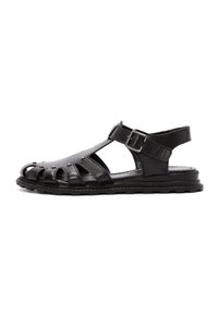 Sandali in pelle nera con design open-toe, lati traforati e fibbia laterale. La suola è strutturata per garantire aderenza e comfort.