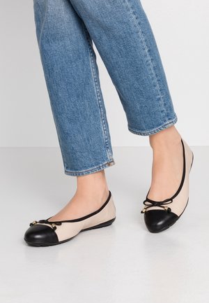 Beige en zwarte ballerina's met afgeronde neuzen, een zwarte rubberen neuskap en dunne zwarte veterstrik aan de voorkant. Glad oppervlak, minimalistisch ontwerp.