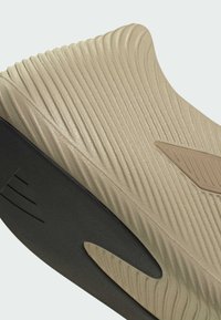 Επάνω μέρος αθλητικού παπουτσιού σε μπεζ χρώμα με ραβδωτή υφή και μαύρη σόλα. Διαθέτει καφέ λεπτομέρεια και αεροδυναμικό σχεδιασμό. Διάφορες αυλακώσεις βελτιώνουν την πρόσφυση.