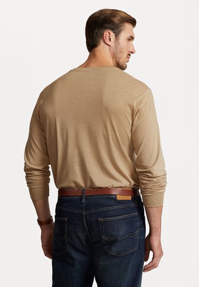 Μπεζ πουκάμισο με μακριά μανίκια και χαλαρή εφαρμογή, από πλεκτό ύφασμα με ριμπ μανσέτες. Συνδυάζεται με σκούρο μπλε τζιν και καφέ δερμάτινη ζώνη.