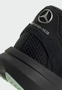 Sort atletik sko med overdel i mesh og ruskind, der har et sølv Mercedes-Benz logo og en struktureret sort gummisål med en let bue.