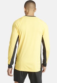 Langärmliges Jersey in leuchtendem Gelb mit schwarzen Seitenpaneelen. Glatte Textur, Rundhalsausschnitt und taillierte Passform, geeignet für Sportaktivitäten.