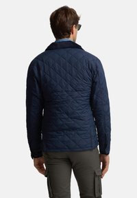 Chaqueta acolchada azul marino con cuello de pana, que presenta una textura suave y detalles de botones. La vista trasera muestra un diseño aerodinámico.