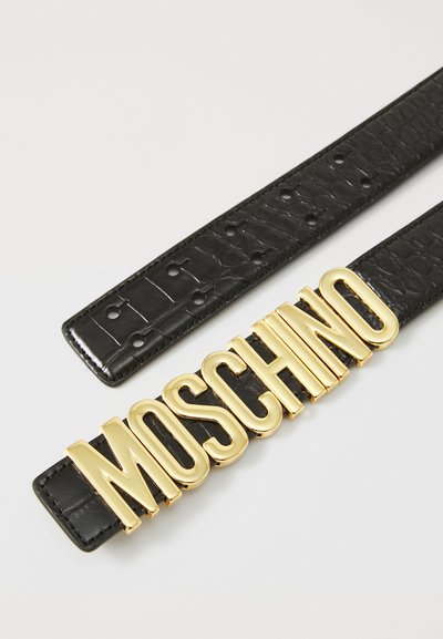 Must mustrips krokodillimustriga, millel on suur kuldne "MOSCHINO" logo pandla. Rihmal on nähtavad suuruseaugud reguleerimiseks.
