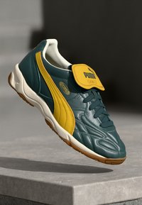 Teal og gul sneaker med en teksturert lær-overdel, polstret tunge, og gummisåle med diamantmønster og preget logo.