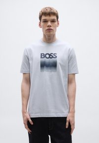 Helehall triiksärk, millel on mustast gradientvärvist "BOSS" graafika. Lühikesed varrukad ja ümara kaelusega pehme, sileda kangaga.