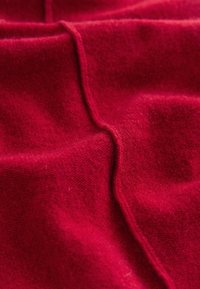 Tissu doux rouge avec des coutures visibles et des plis, montrant la texture et les fibres fines en gros plan.