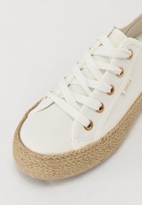 Hvite lerrets sneakers med flette jute såle, med gulldetaljer og flate bomullssnører. Minimalistisk design og rund tåform.