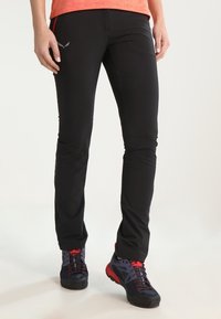 Pantalon d'extérieur noir en tissu léger, avec une coupe slim, des poches à fermeture éclair et des accents rouges contrastants sur les coutures latérales.