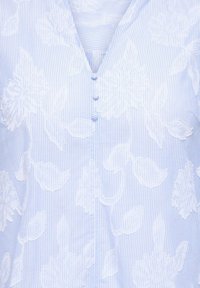 Svetlomodrá a bielo pruhovaná blúzka s bielou kvetinovou výšivkou a tromi malými gombíkmi potiahnutými tkaninou na výstrihu.