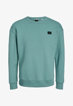 Hellblau-grüner Pullover aus weichem Stoff. Verfügt über einen Rundhalsausschnitt, gerippte Bündchen und ein kleines schwarzes Markenetikett auf der linken Vorderseite.
