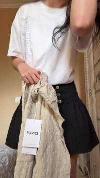 Άτομο που φοράει λευκό πουκάμισο και μαύρη φούστα, κρατώντας μπεζ υφασμάτινο ρούχο με ορατή ετικέτα μάρκας "ONLY" σε εσωτερικό χώρο.
