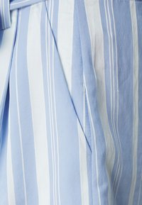 Tessuto blu chiaro con strisce verticali in diverse tonalità e una texture liscia. Strisce bianche molto evidenti creano un motivo sottile.