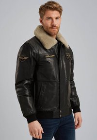 Chaqueta de cuero negra con un cuello de borrego beige, cierre de cremallera y parches inspirados en el estilo militar en el pecho y las mangas. Puños y dobladillo acanalados.