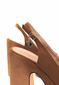 Sandali alti in suede marrone con plateau, design open-toe e dettagli in metallo dorato, dotati di un charm attaccato alla cinghia alla caviglia.