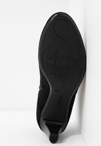 Semelle de chaussure à talon haut en daim noir avec motif décoratif, marque "Gabor", et un talon élancé présenté sur un fond blanc d'angle.