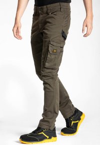 Pantalons cargo en vert olive, avec plusieurs poches, une coupe slim et un matériau durable. Associés à des chaussures noires et jaunes.