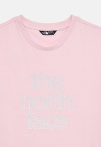 Svijetloružičasta pamučna majica s natpisom "the north face" u podebljanom, teksturiranom fontu, a ispod njega bijeli naglasak "NEVER STOP EXPLORING".