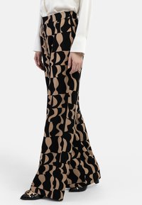 Schwarze und beige abstrakt gemusterte Schlaghosen aus glattem Stoff, mit hoher Taille und Seitentaschen. Akzentuiert durch schwarze Schuhe.