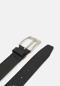 Ceinture en cuir noir avec une boucle en métal argenté, offrant une texture lisse, plusieurs trous d'ajustement, et une marque discrète sur la boucle.