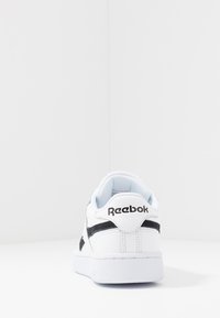 Biele tenisky s čiernymi akcentmi, vyrobené z kože a syntetických materiálov. Majú textúrovanú podrážku a vypchatý golier s brandingom Reebok.