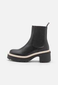 Černé kotníkové boty s hladkým koženým povrchem, texturovanými bočními panely a masivním černým podpatkem. Bílá kontrastní podrážka zvýrazňuje design.