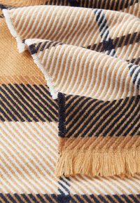 La sciarpa in misto lana tessuta presenta un motivo a scacchi con strisce alternate in beige, crema e blu marino, rifinita con un bordo con frange.
