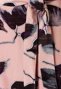 Blumenkleid aus weichem rosa Stoff, mit großen dunkelvioletten Blättern, die weiße Umrandungen haben. Enthält ein vorderes Bindedetail.