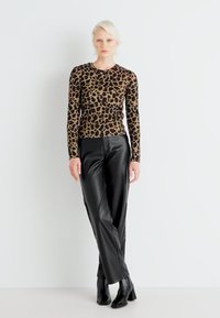 Halenka s leopardím vzorem s dlouhým rukávem, spárovaná s černými koženými kalhotami a botami na vysokém podpatku. Hladké textury a přiléhavá silueta.