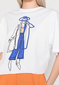 Bílý tričko s modrým a černým liniovým kreslením postavy ve stylovém oblečení, s oranžovými akcenty, pohodlný střih a měkká textura.