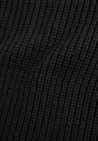 Gros plan sur un tissu noir texturé avec des rainures verticales, mettant en avant une apparence douce et tricotée. Aucun motif distinct ou objet présent.