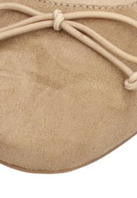 Primer plano de un zapato de ante beige, con una punta redondeada y un lazo atado de acento con cordones finos, textura suave y detalles de costura sutiles.